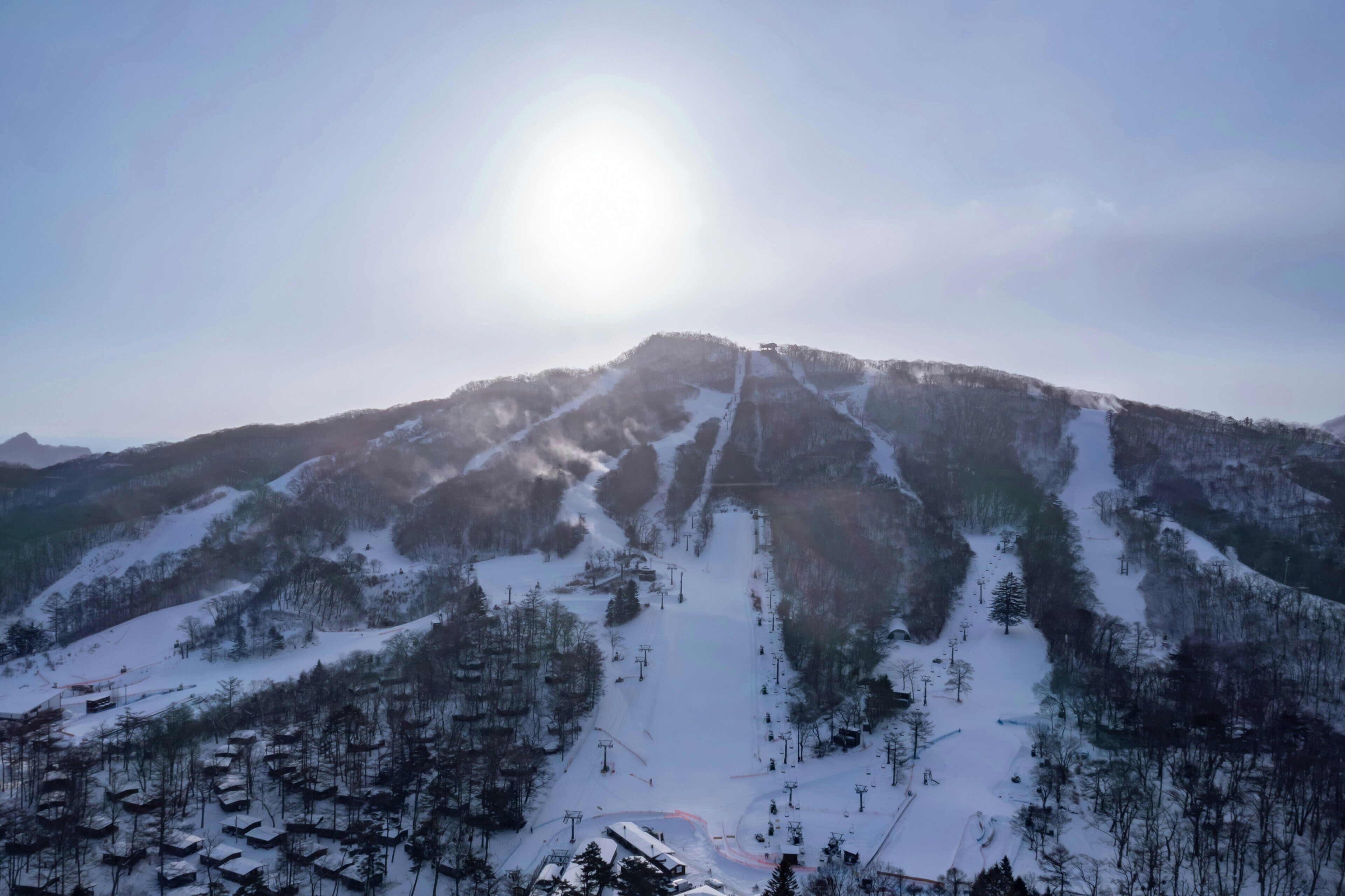 A snow-covered mountain with ski slopes, a clear sky, and a bright sun.