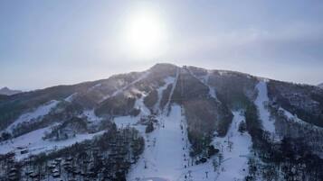 A snow-covered mountain with ski slopes, a clear sky, and a bright sun.