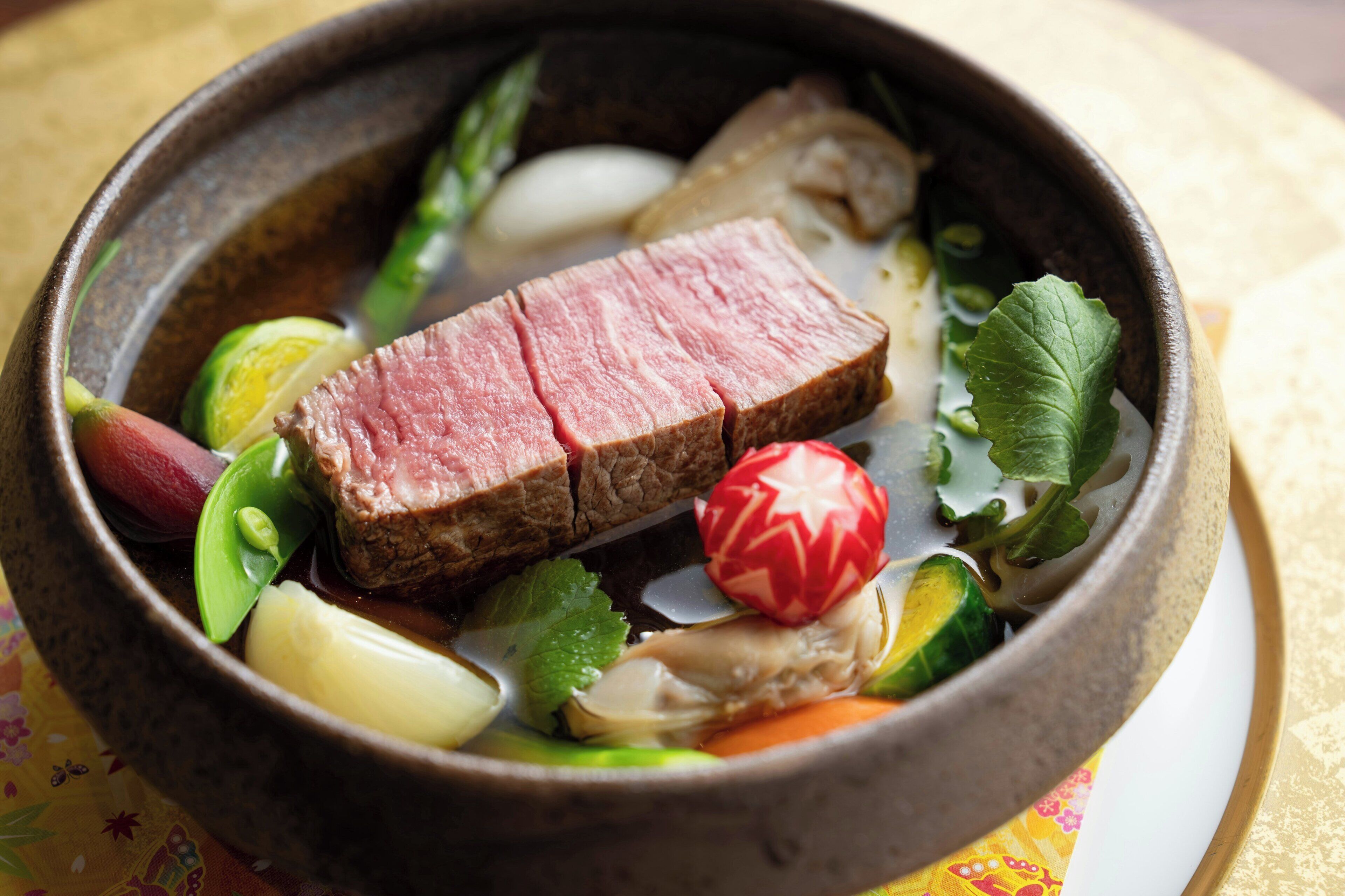 A bowl of beef with vegetables and a red decorative item.