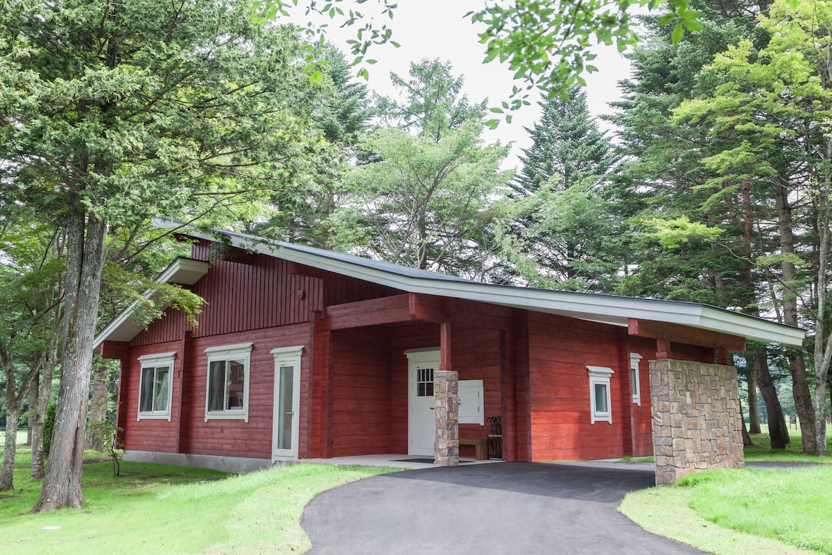 A red wooden house with a stone pillar, surrounded by trees.
