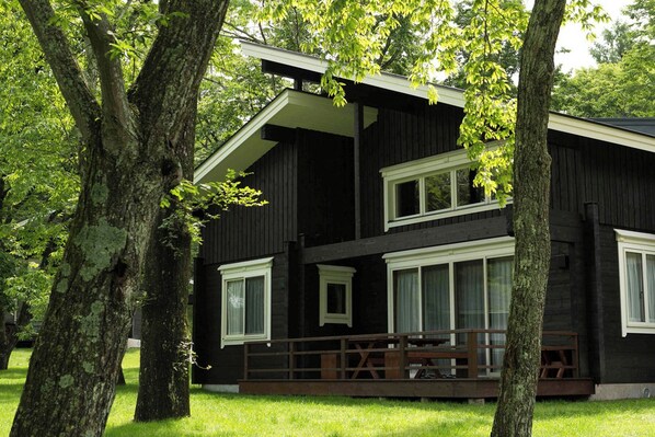A two-story wooden cabin with a balcony, surrounded by trees.