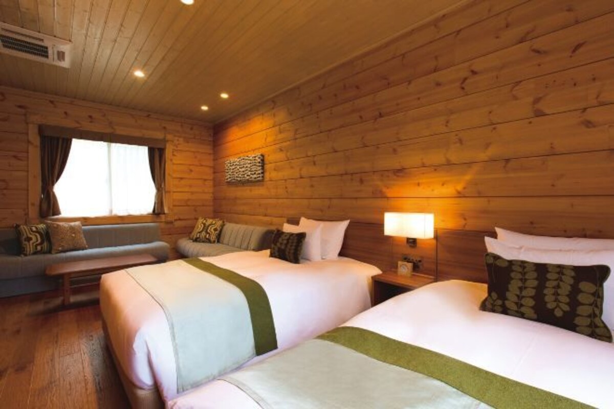 A wooden cabin room with two beds, a sofa, and a window.