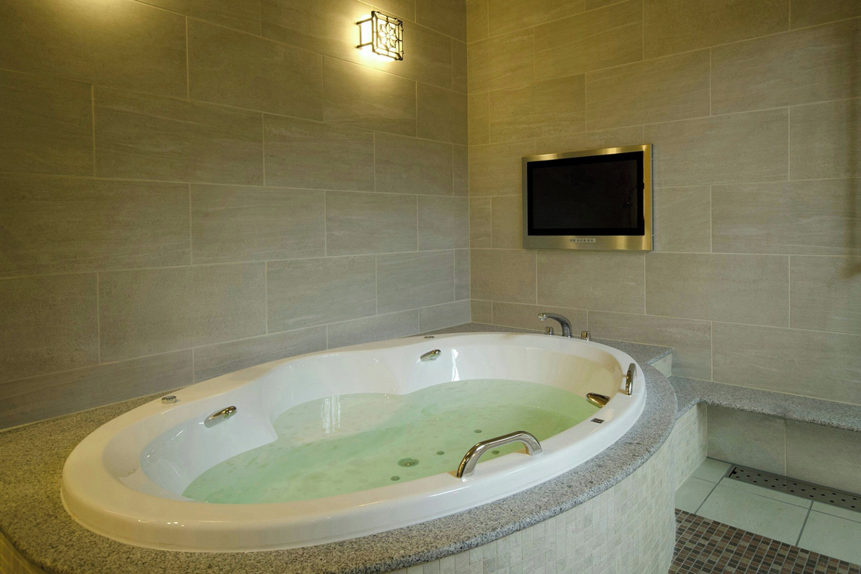 A modern bathroom with a freestanding bathtub, a wall-mounted TV, and a light fixture.
