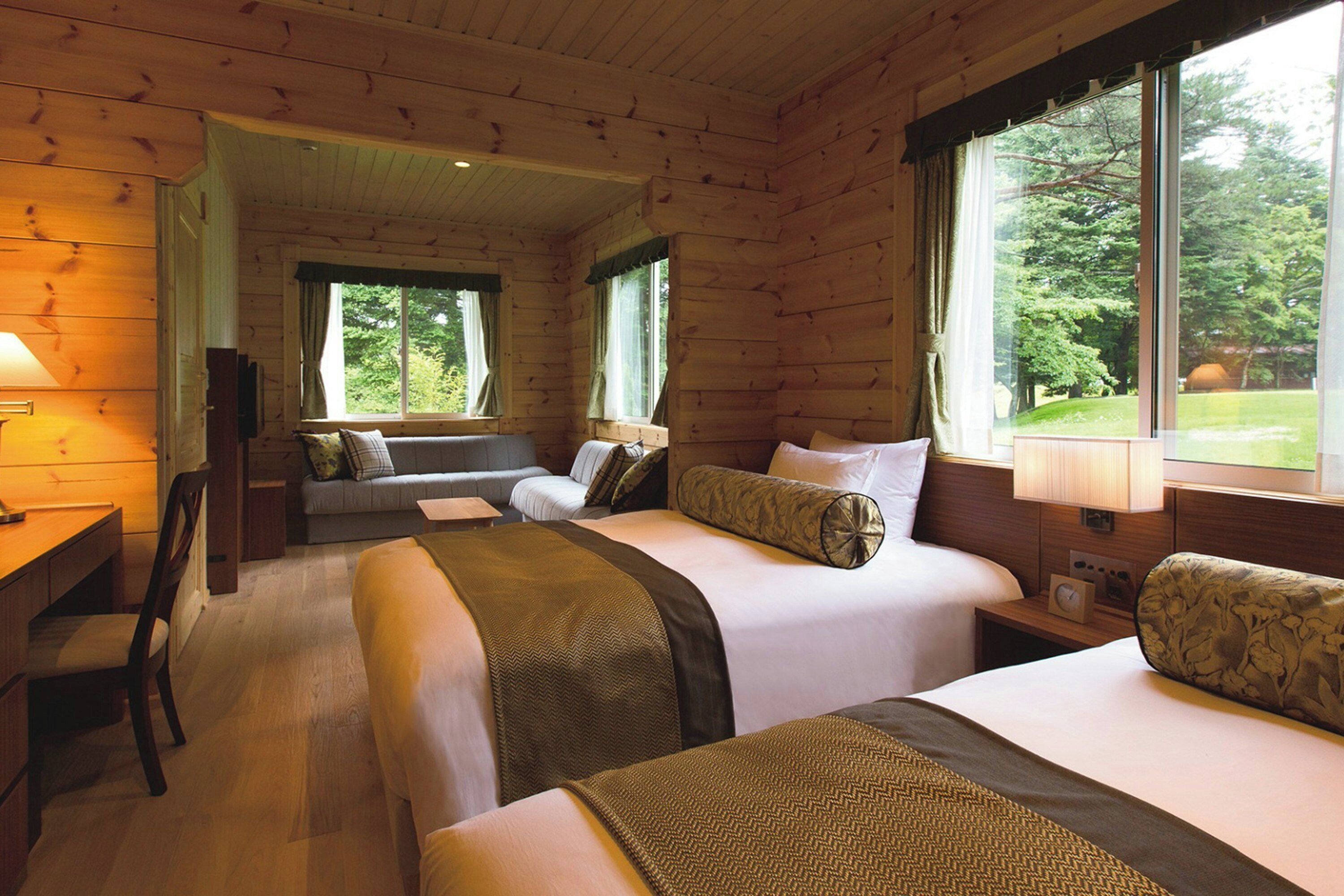 Een kamer in chaletstijl met twee bedden, een bureau en een raam met uitzicht op bomen.