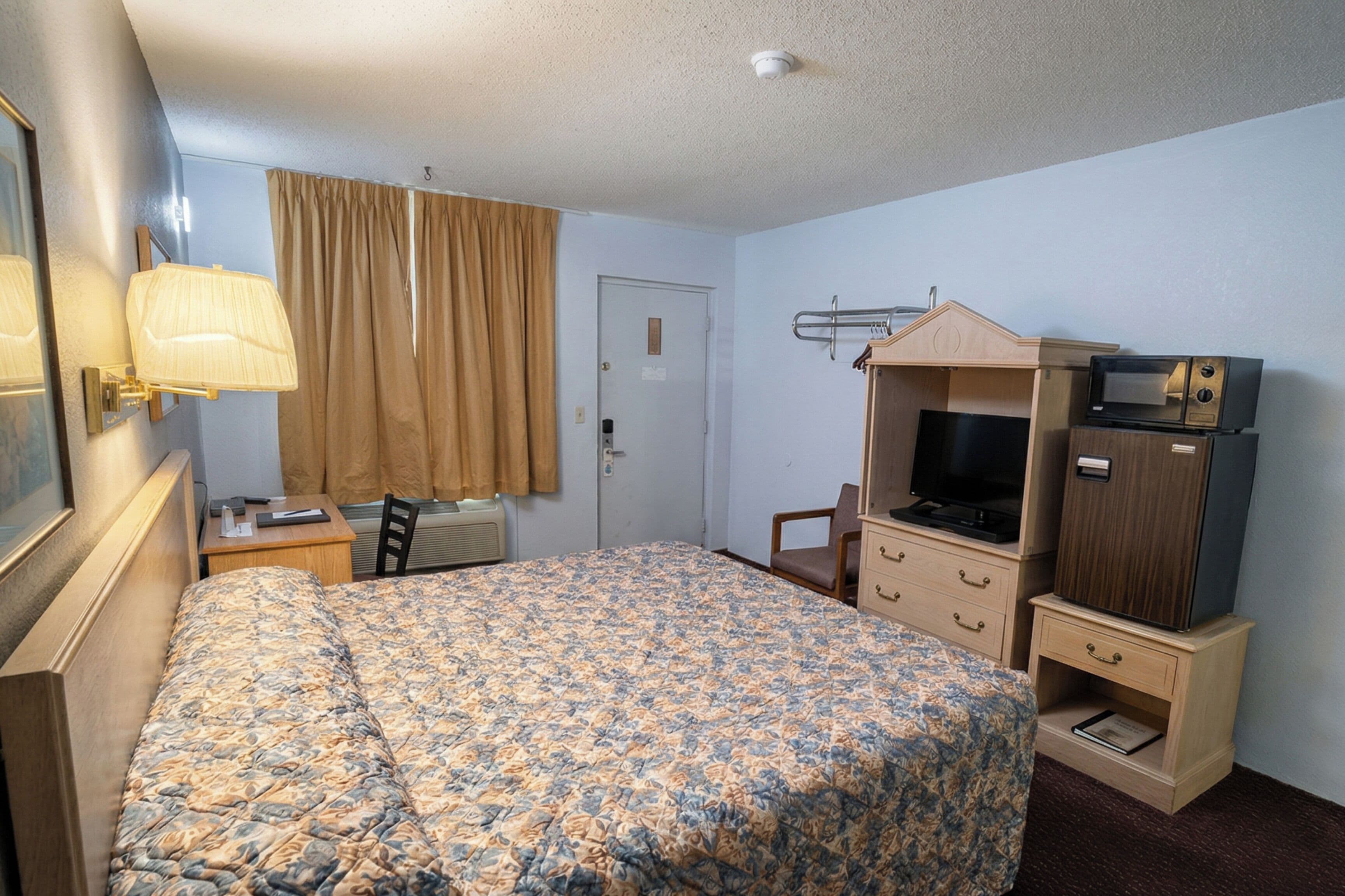 A hotel room with a bed, a desk, a chair, a television, and a small cabinet.