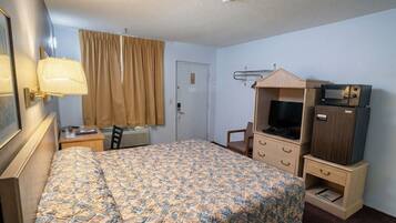 A hotel room with a bed, a desk, a chair, a television, and a small cabinet.