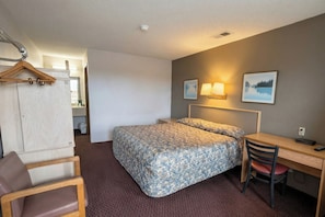A hotel room with a bed, desk, chair, and a wardrobe.
