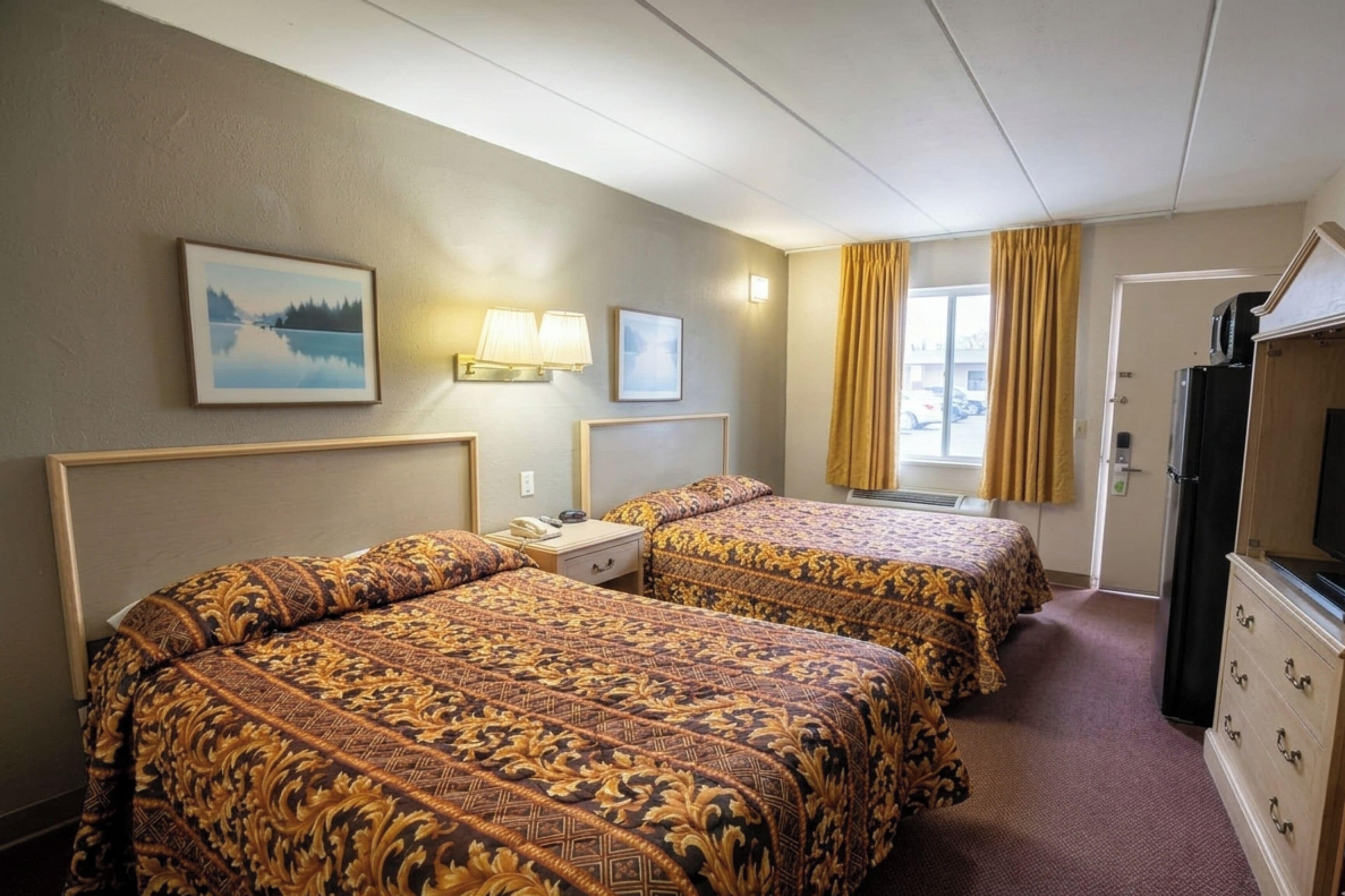 A hotel room with two beds, a desk, a television, and a window with curtains.