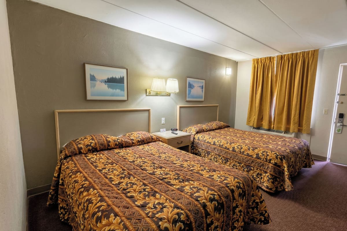 Ein Hotelzimmer mit zwei Betten, einem Nachttisch, einer Lampe und einem Fenster mit Vorhängen.