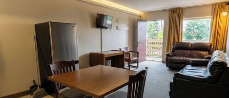 A living area with a wooden table, chairs, a sofa, a television, and a refrigerator.