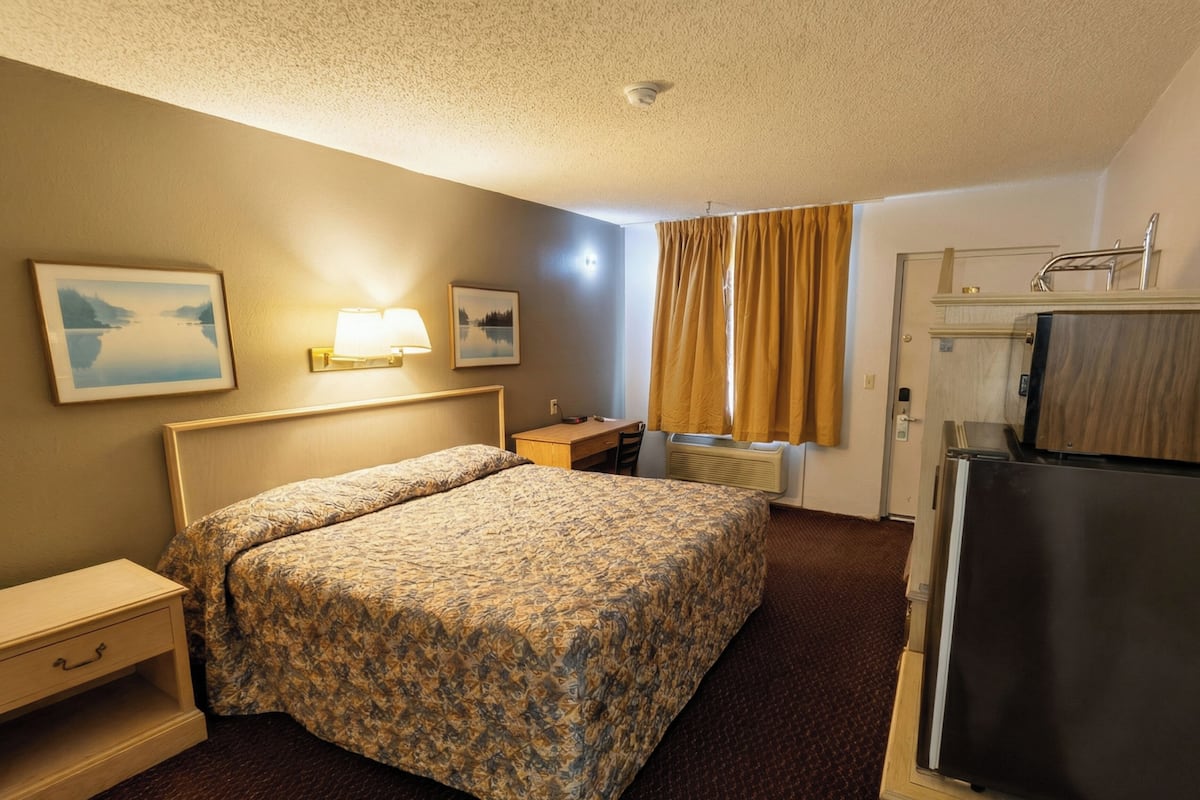 Ein Hotelzimmer mit Bett, Nachttisch, Lampe und einem Kühlschrank.