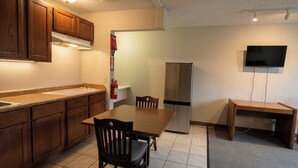 A kitchen with wooden cabinets, a stainless steel refrigerator, a dining table with chairs, and a TV mounted on the wall. - Lake Erie Lodge Oregon OH (Curtice)