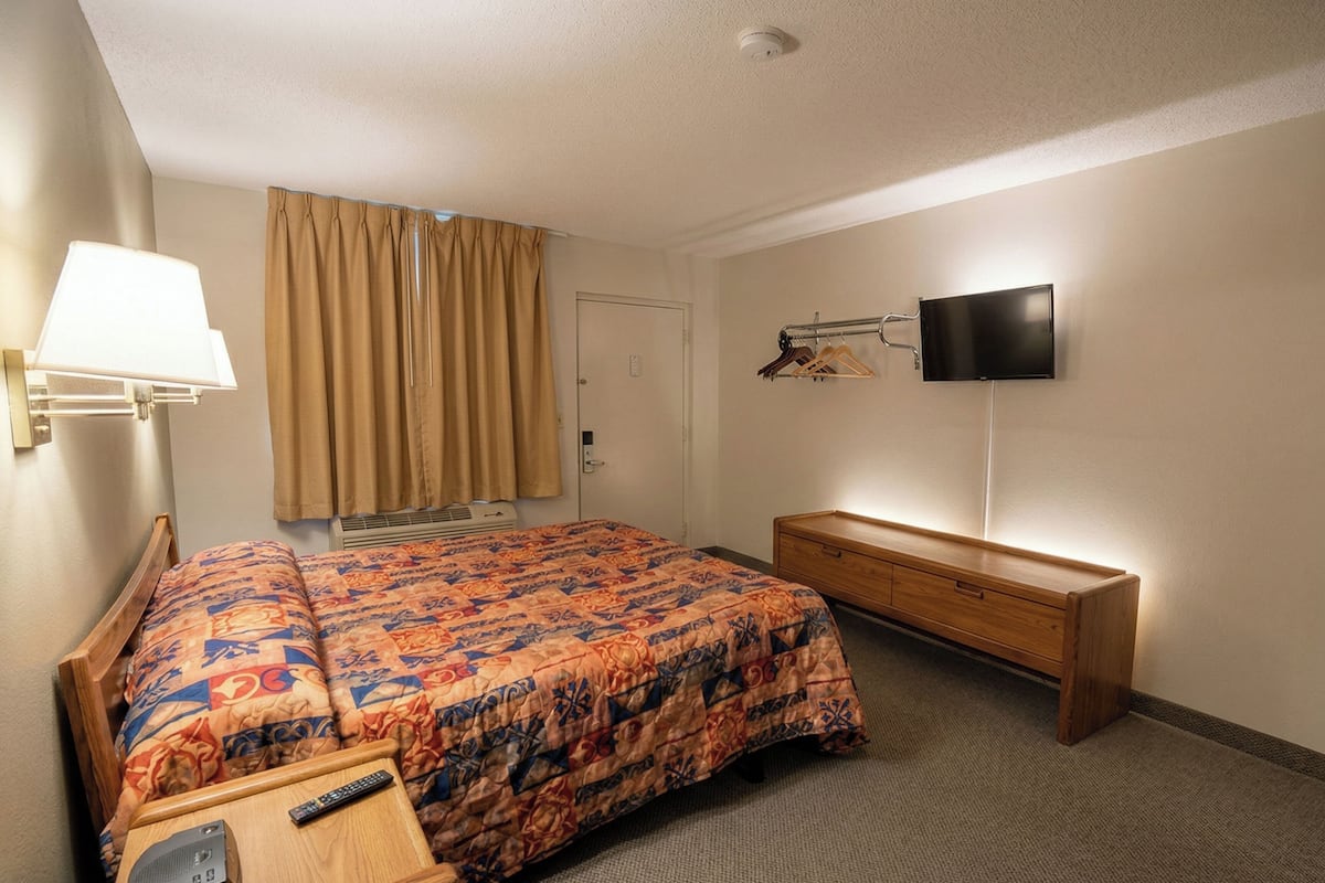 Ein Hotelzimmer mit Bett, Nachttisch, Lampe, Fernseher und einem Holzschrank.