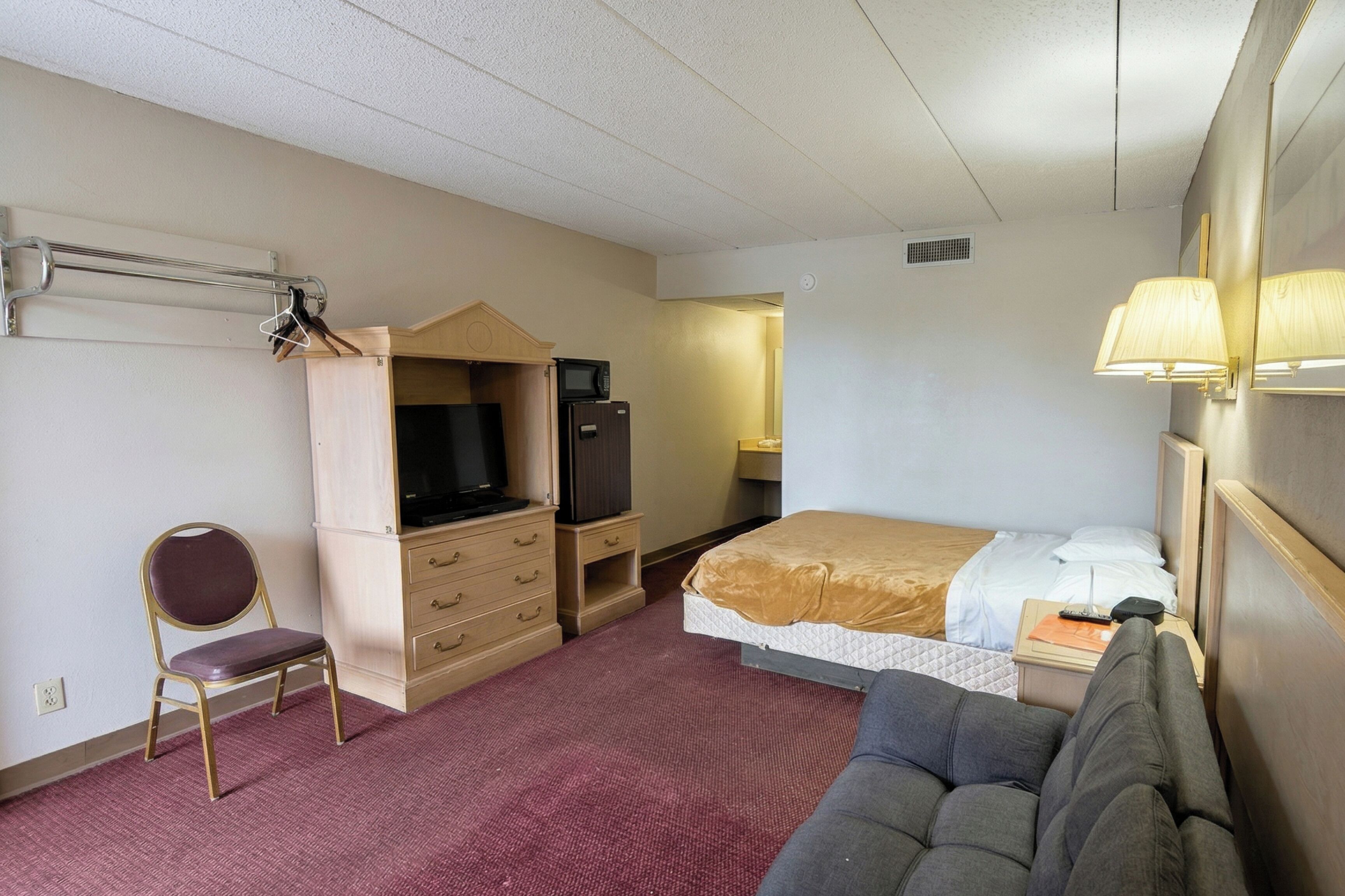 A hotel room with a bed, a desk with a computer, a chair, a television, and a microwave.