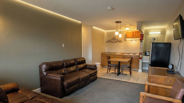 A living room with a brown leather sofa, a dining table with chairs, a kitchen area with wooden cabinets, and a flat-screen TV mounted on the wall. - Lake Erie Lodge Oregon OH (Curtice)