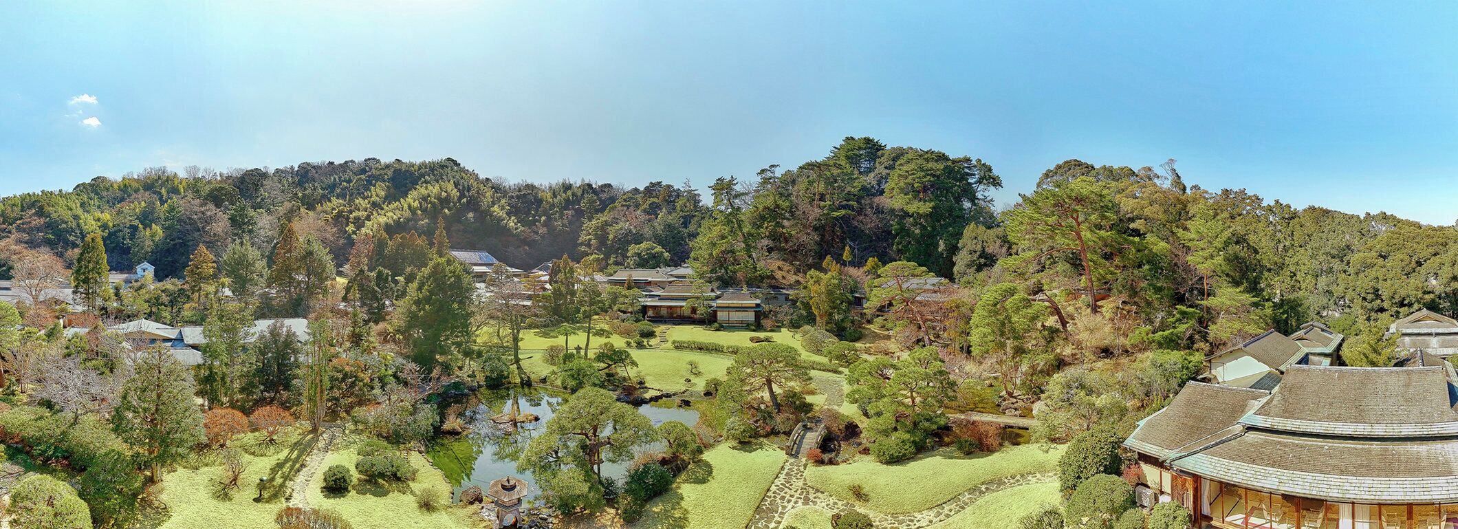 A traditional Japanese garden with a pond, pathways, and buildings with tiled roofs.