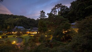 Un edificio de estilo japonés tradicional rodeado de un bosque frondoso, con un jardín cuidado y un campo de golf en el fondo.