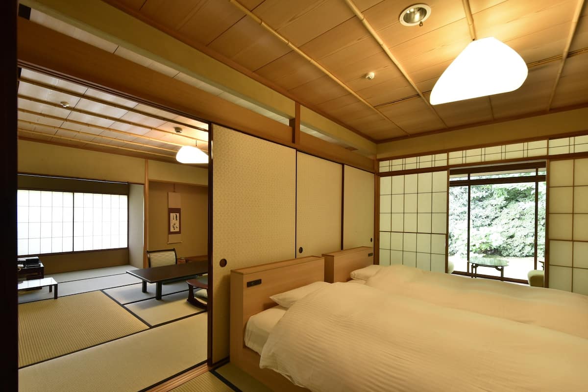 A traditional Japanese-style room with tatami flooring, a low wooden bed, a sliding door, and a view of greenery outside.