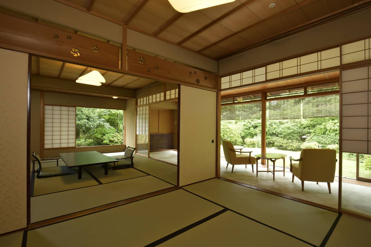 A traditional Japanese room with tatami flooring, sliding doors, and a view of greenery.