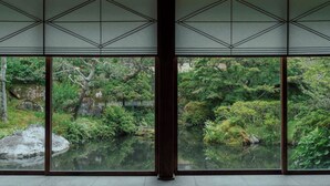 Una habitación japonesa tradicional con suelo de tatami, un celosía de papel y vistas a un jardín con estanque.