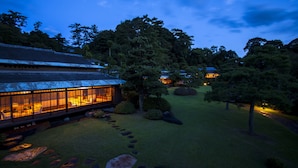 A traditional Japanese-style building with a large glass facade, surrounded by a well-maintained garden with stepping stones and trees. - Sanyo-so (Izunokuni)