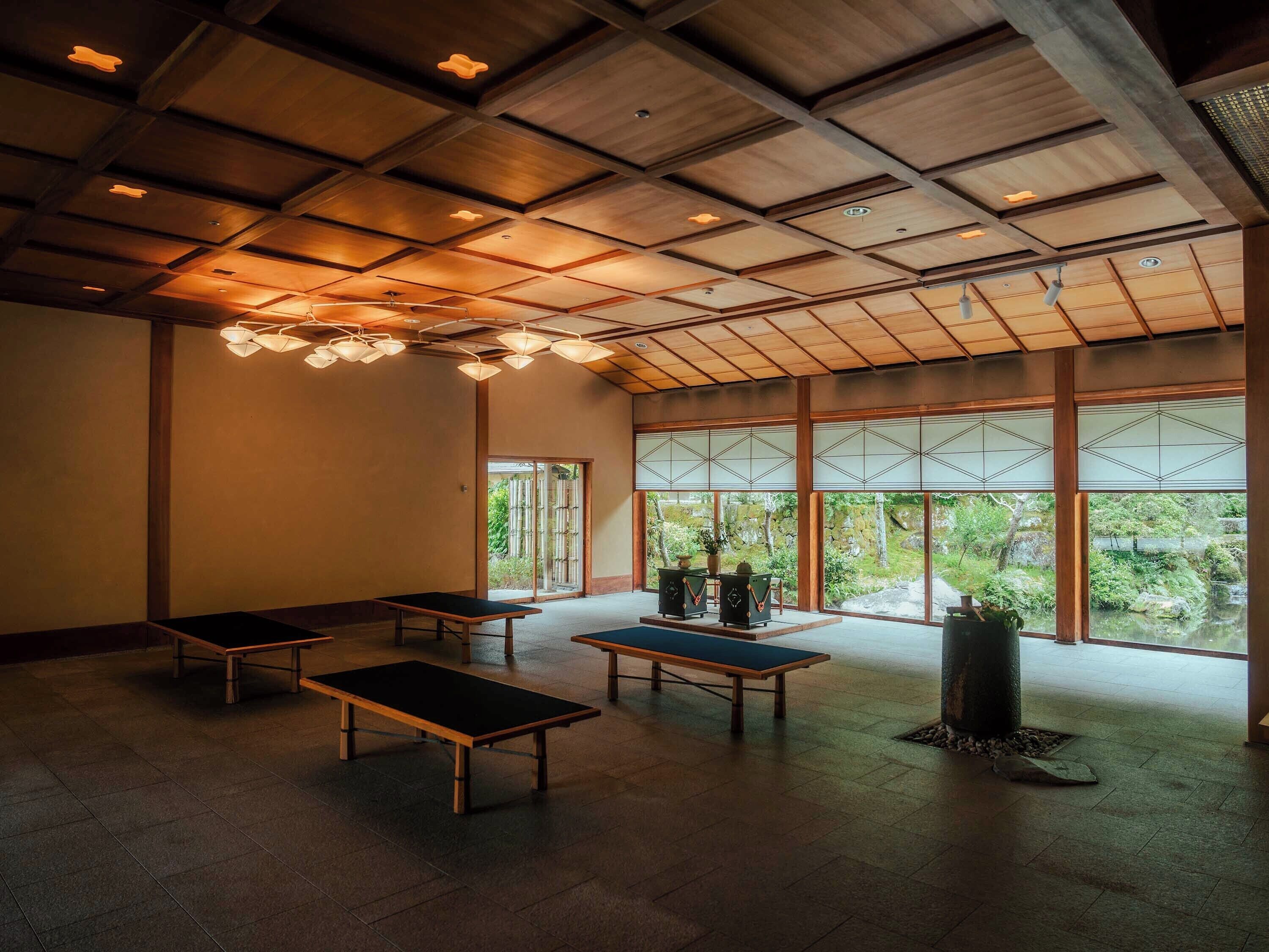 A spacious room with a high ceiling and large windows, featuring traditional tatami mats and low tables.