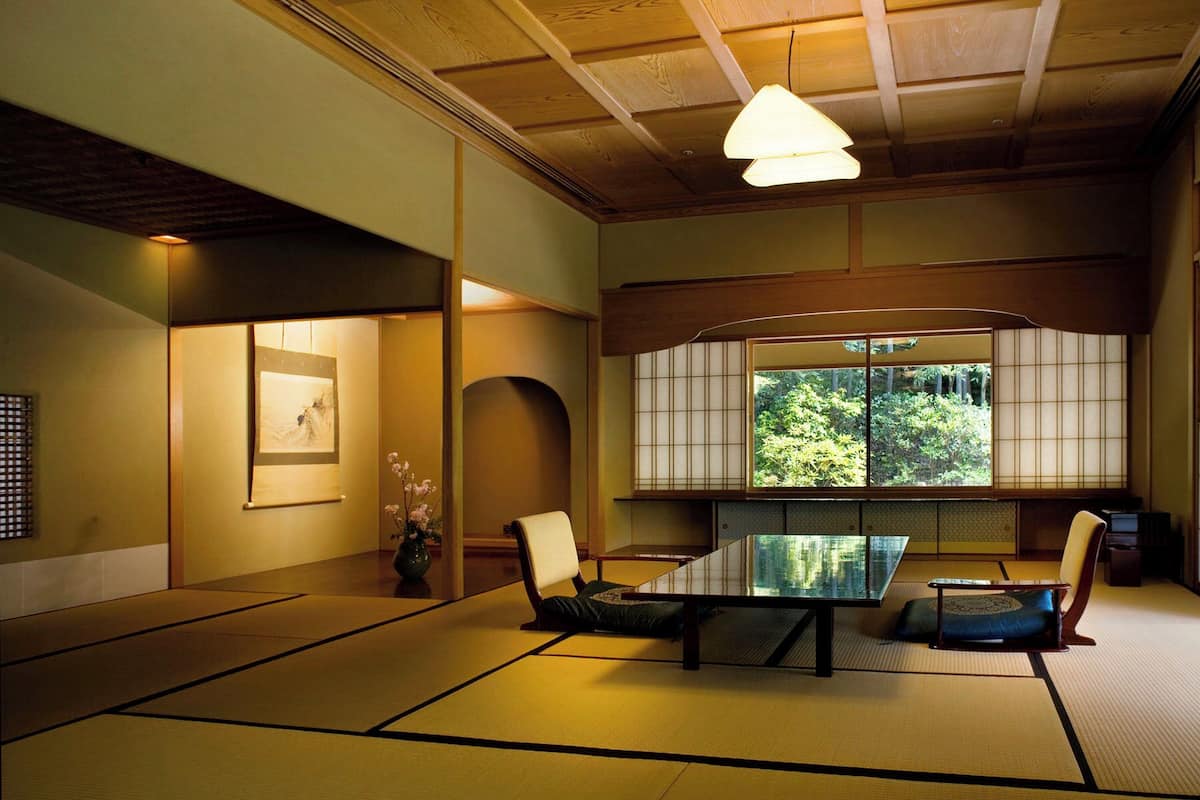 A traditional Japanese room with tatami flooring, a low table, and a view of greenery through a shoji screen.