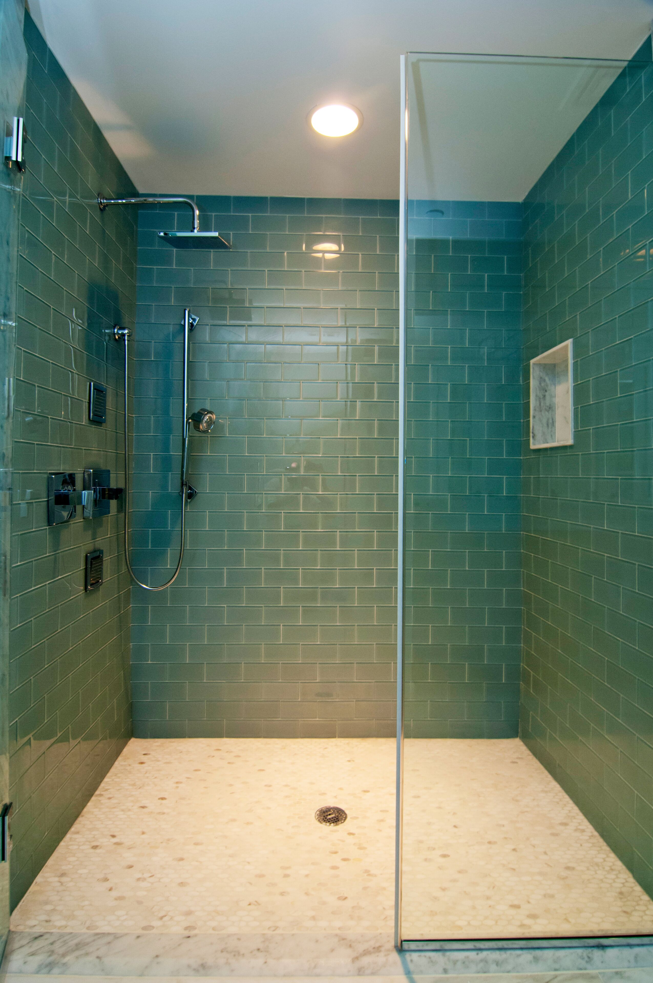 Une douche fermée par des parois de verre, avec un sol carrelé et une seule pomme de douche.