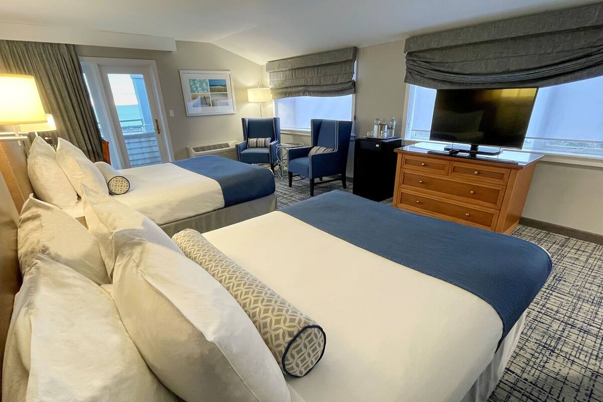 A hotel room with two beds, a desk, a television, and a window with curtains.