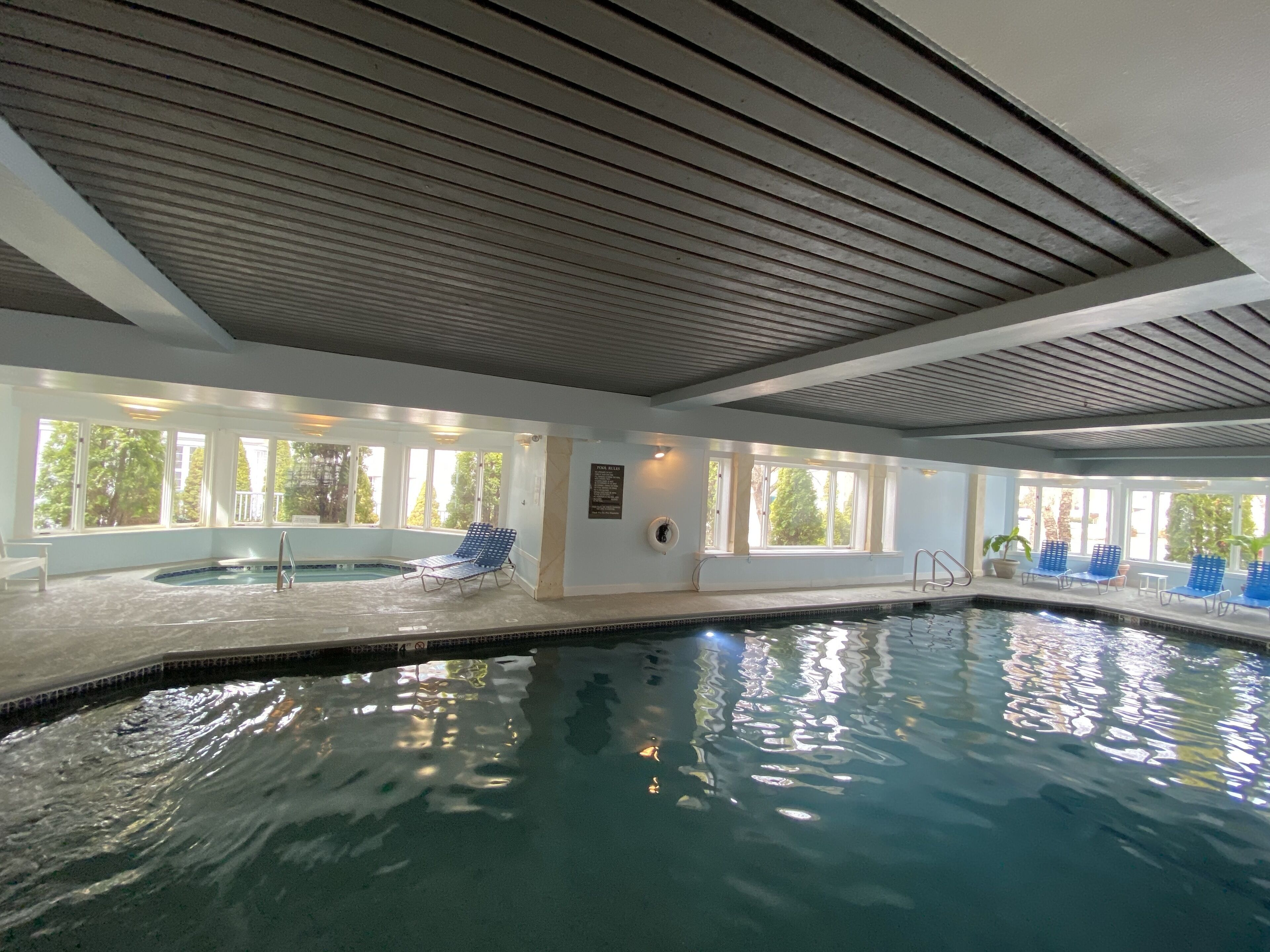 An indoor swimming pool with clear water, surrounded by blue lounge chairs and a sunlit ceiling.