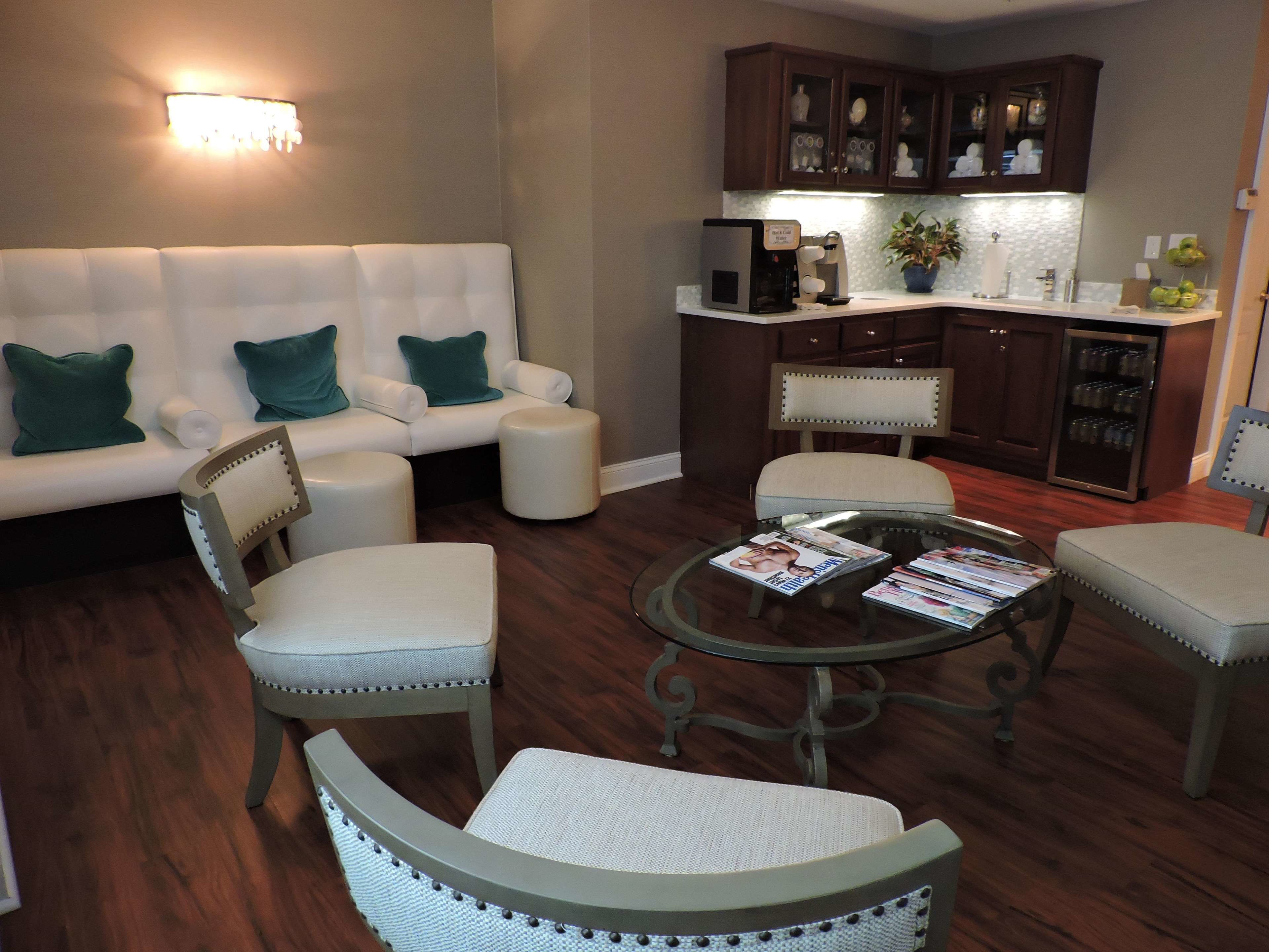 A living room with a sofa, chairs, a coffee table, and a kitchen area with cabinets and a refrigerator.