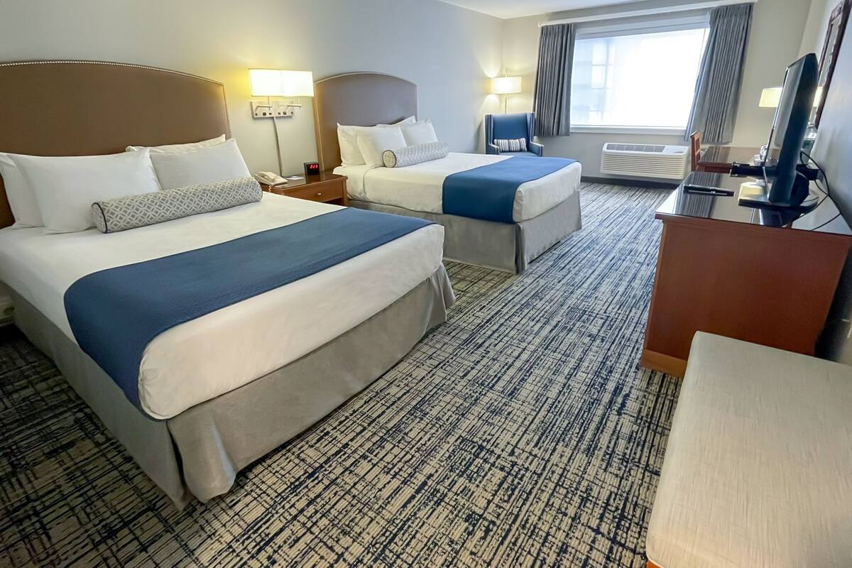 A hotel room with two beds, a desk, a chair, and a large window with curtains.