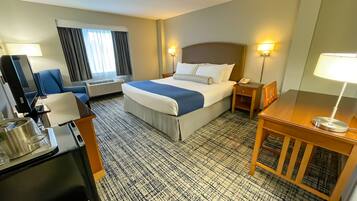 A hotel room with a bed, a desk, a chair, a TV, a lamp, and a window with curtains.