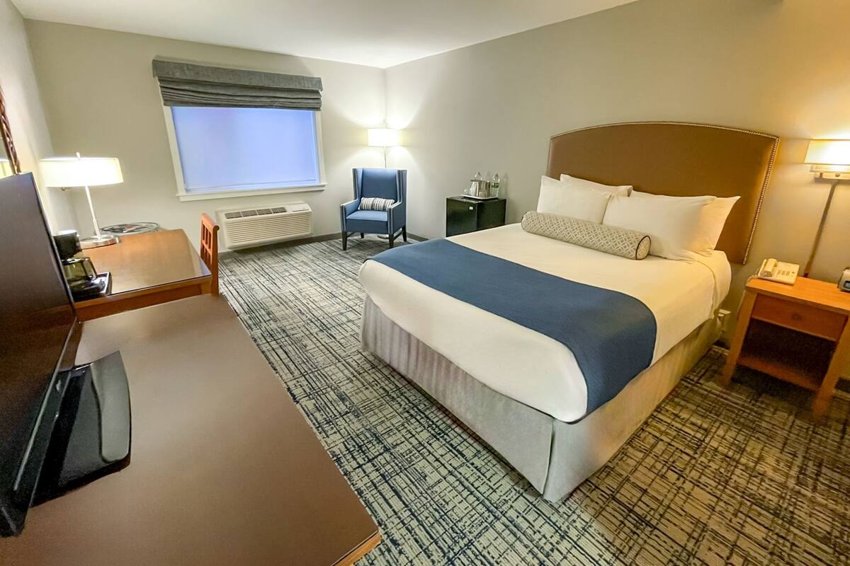 A hotel room with a bed, a desk, a chair, a window, and a nightstand.