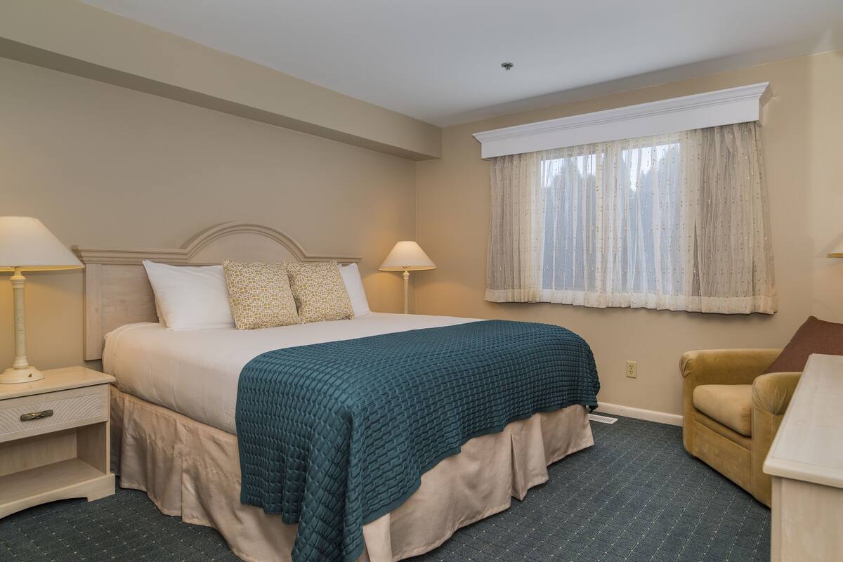 A hotel room with a bed, two bedside tables, a chair, and a window with curtains.