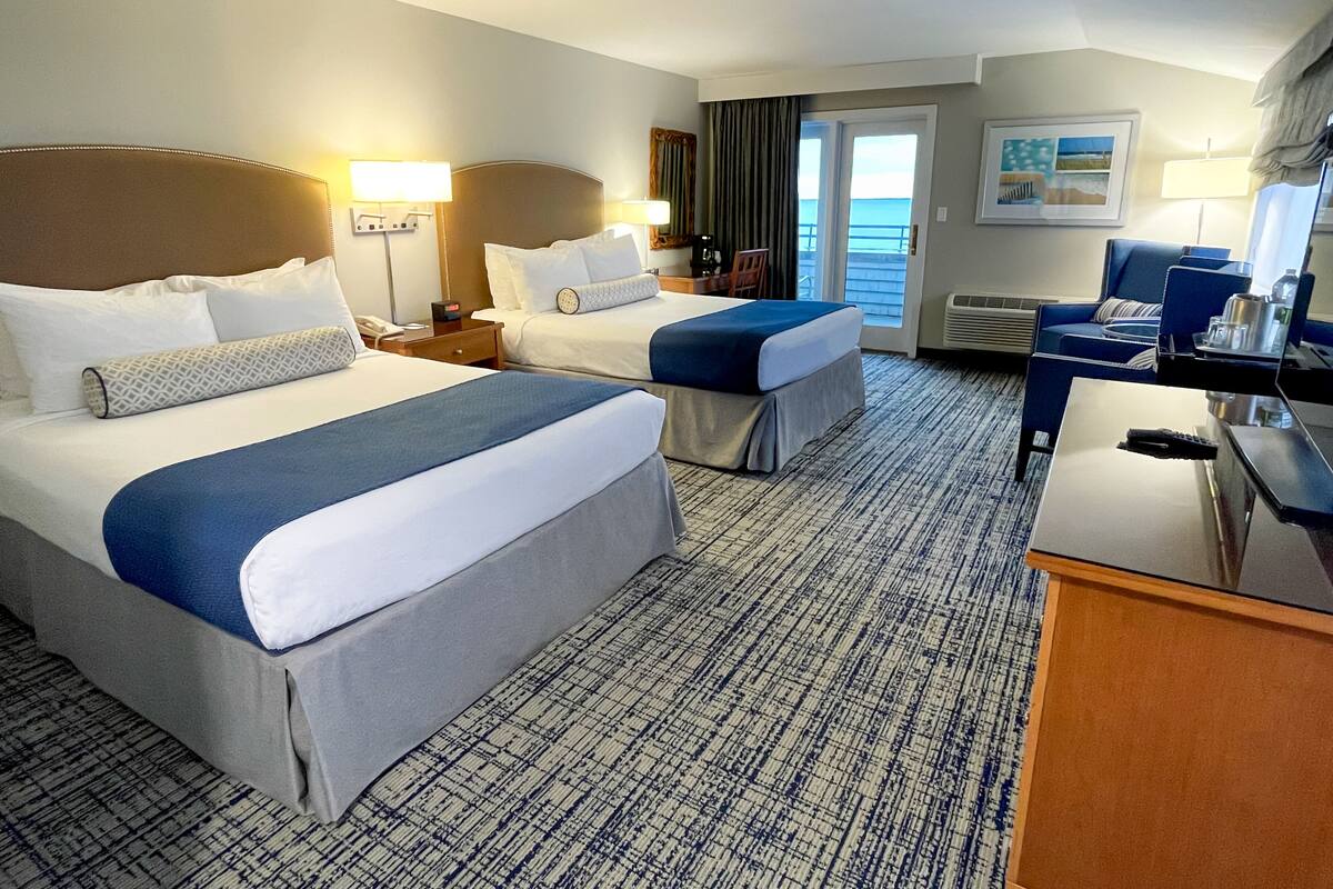 A hotel room with two beds, a desk, a chair, a lamp, and a view of the ocean.