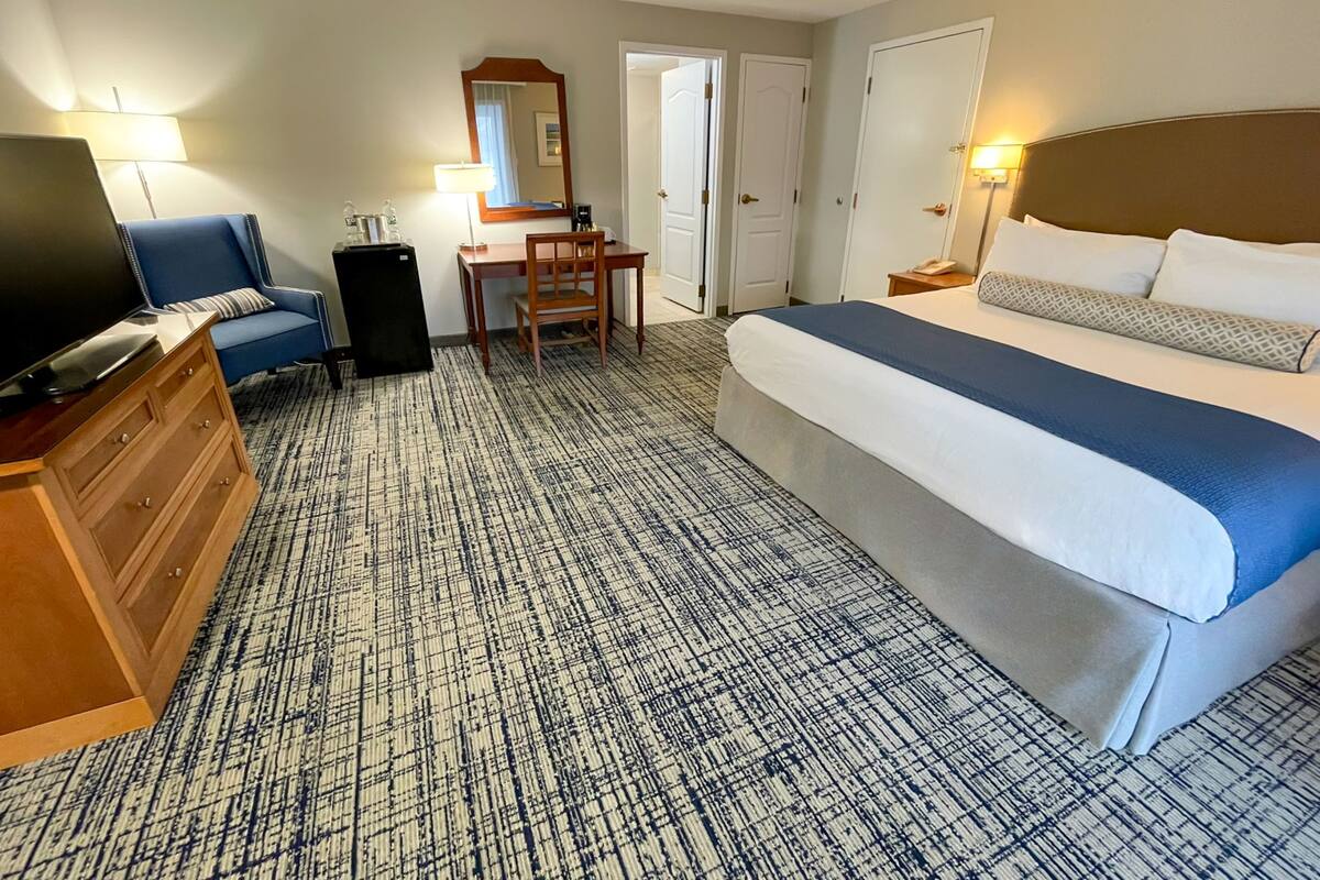 A hotel room with a large bed, a desk with a chair, a television, and a dresser.