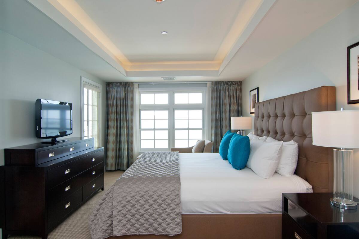 A hotel room with a large bed, a dresser with drawers, a television on the dresser, and a window with curtains.