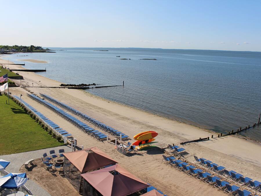 A beachside hotel with rows of blue chairs and umbrellas, a lifeguard tower, and a sandy beach.