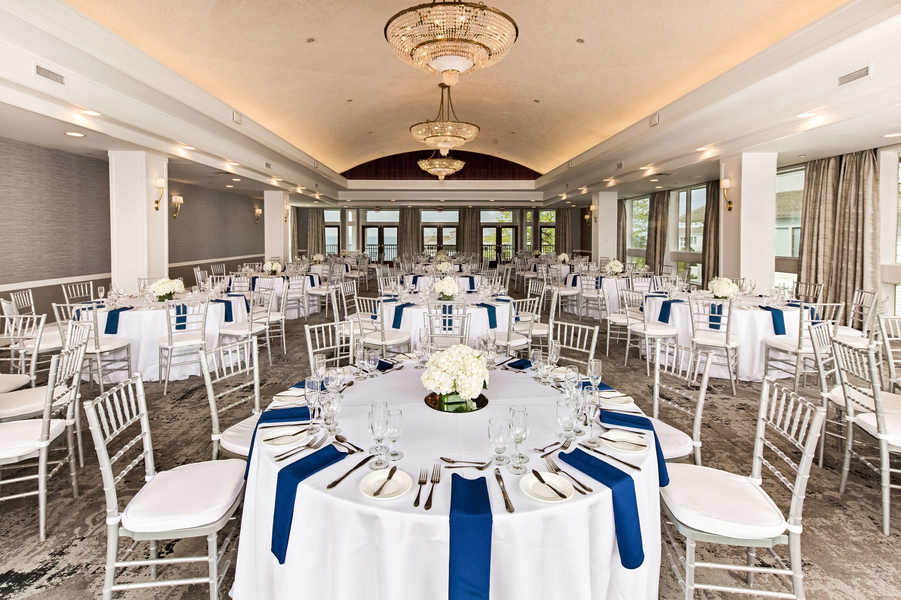 A banquet hall with round tables, white chairs, and blue sashes.