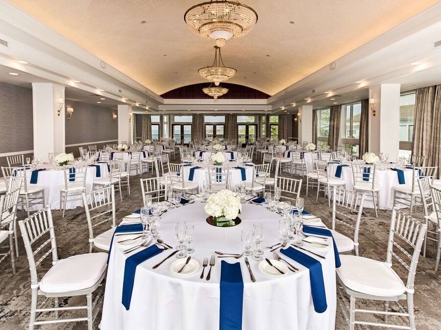 A banquet hall with round tables, white chairs, and blue sashes.