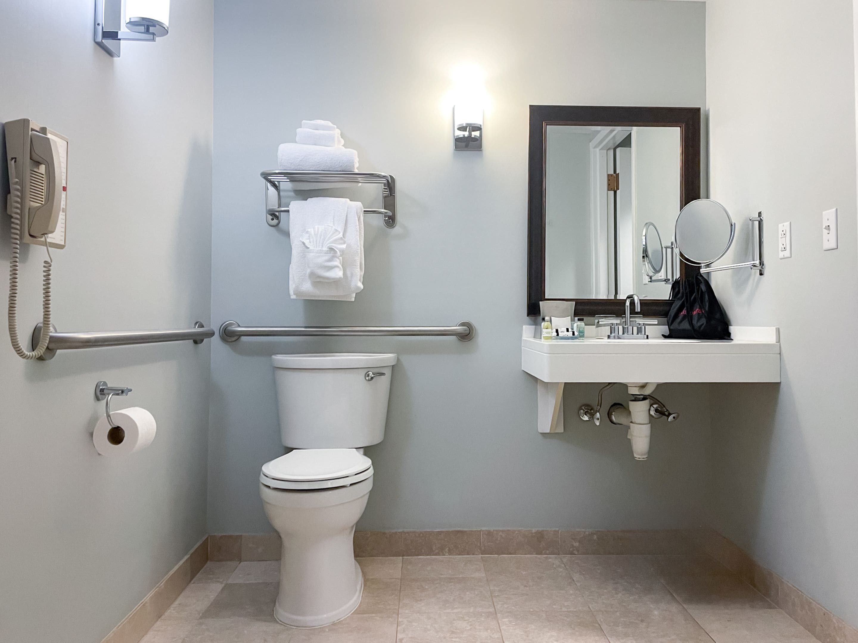 Un baño moderno con inodoro, baranda, toallero, lavamanos con espejo y teléfono.