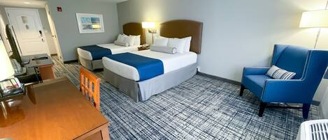 A hotel room with two beds, a desk, a chair, and a patterned carpet.