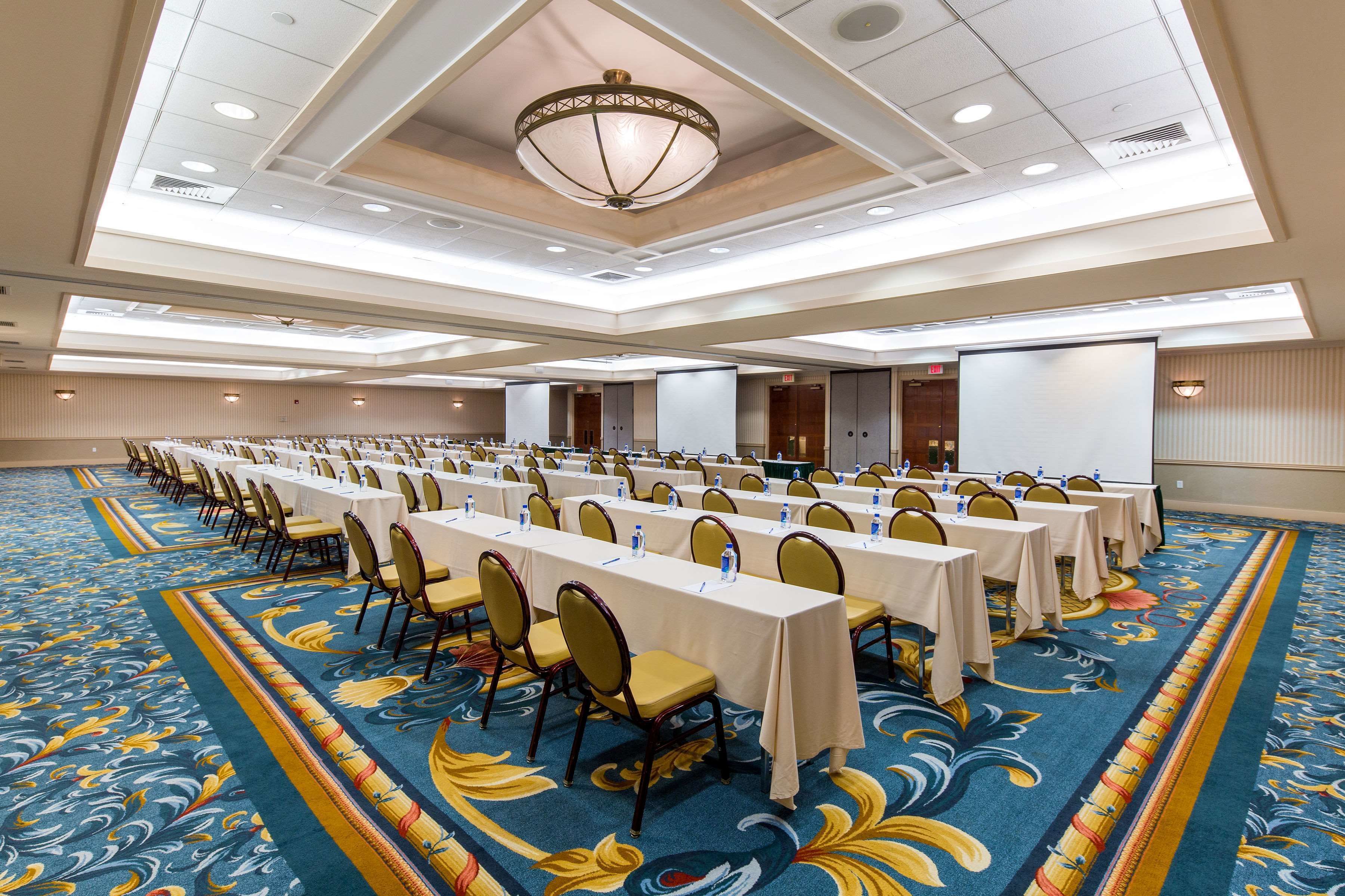 A conference room with long tables and chairs, carpeted floor, and a ceiling with recessed lighting and a chandelier.