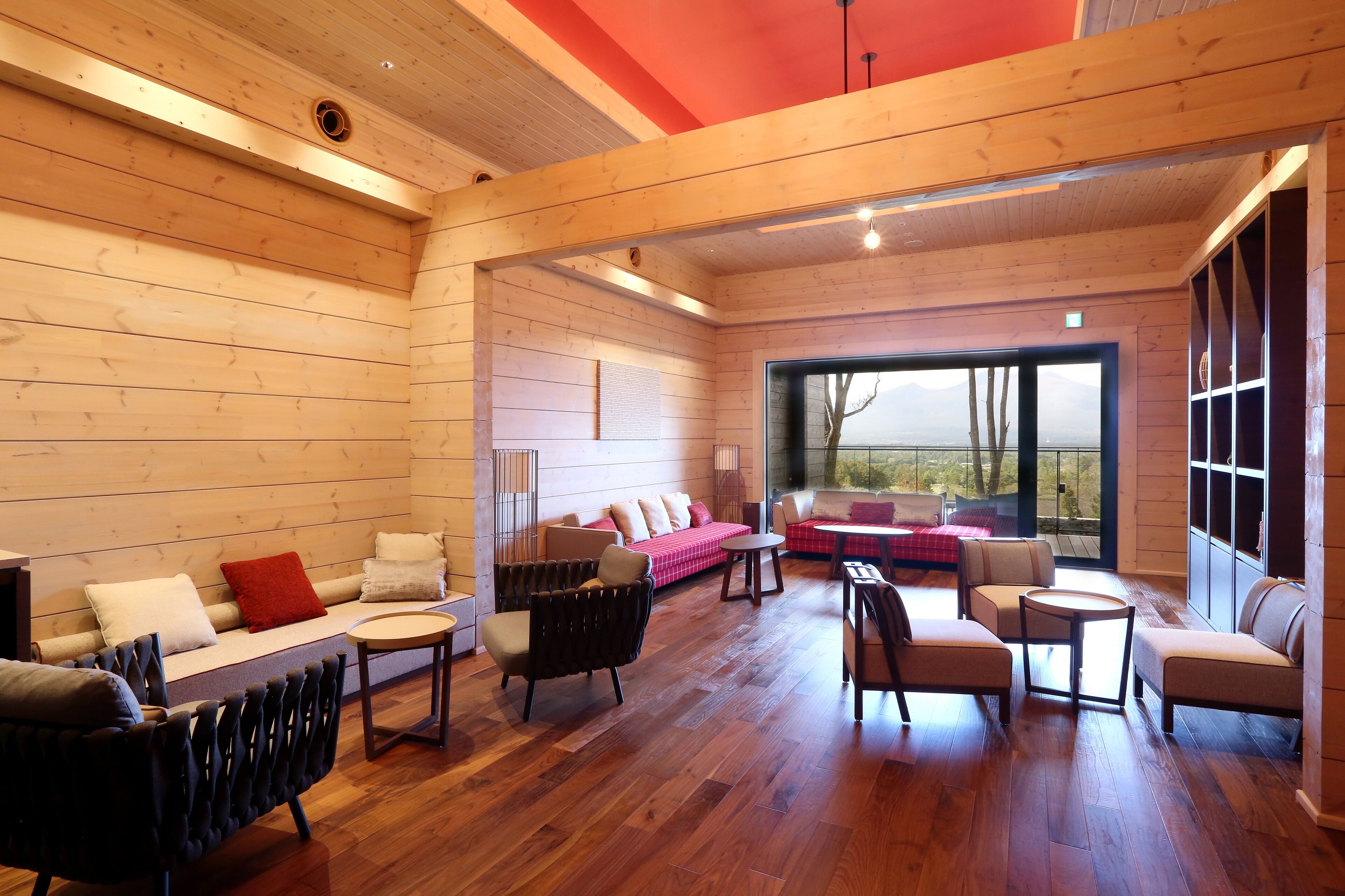 A spacious room with wooden walls and floors, featuring a sofa, chairs, a small table, and a large window offering a view of the outdoors.