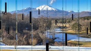 A view through large windows of a mountain landscape, including a snow-capped peak, trees, and a river. - Karuizawa Asama Prince Hotel (Karuizawa)