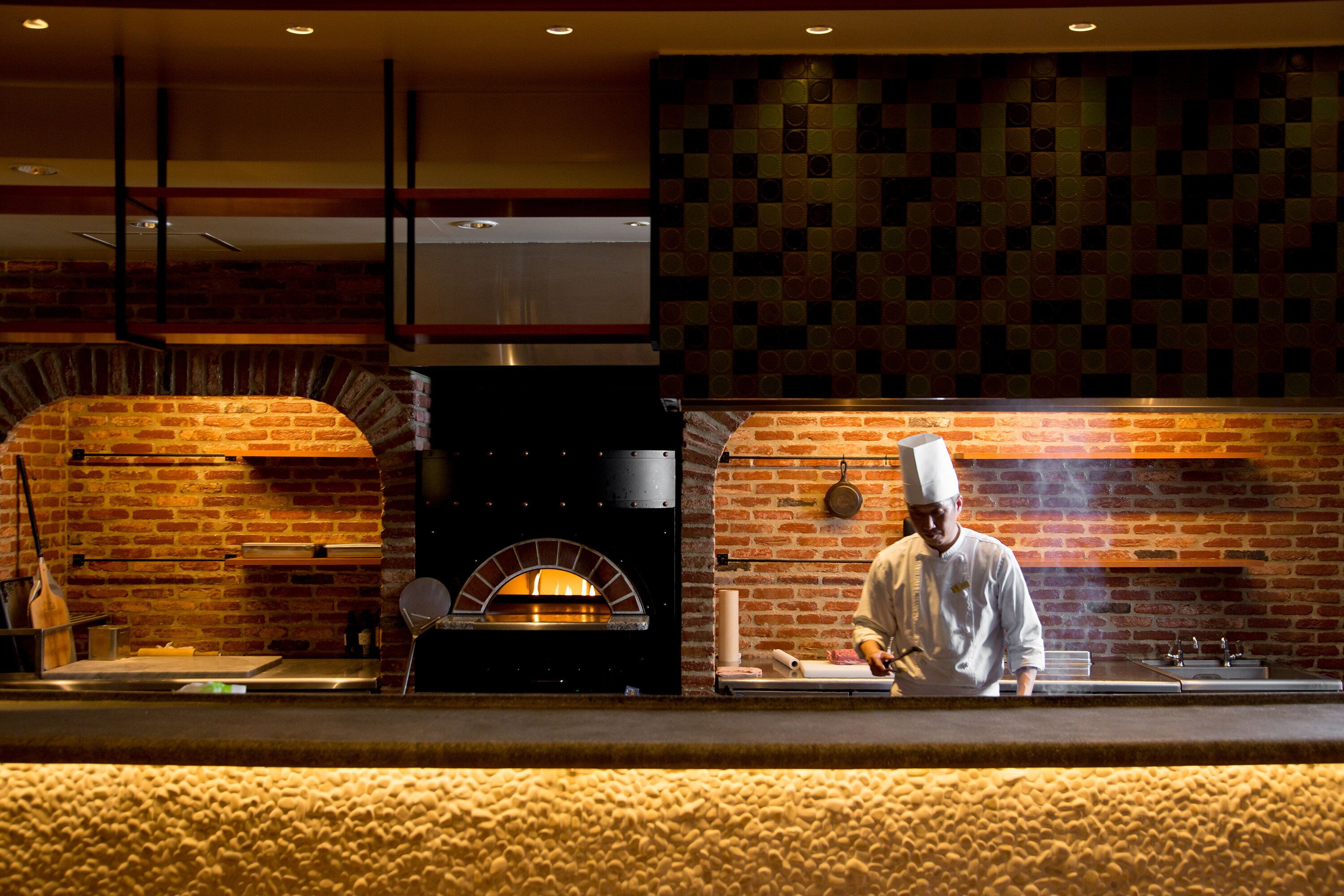 A chef preparing food in a kitchen with a brick wall and a brick oven.