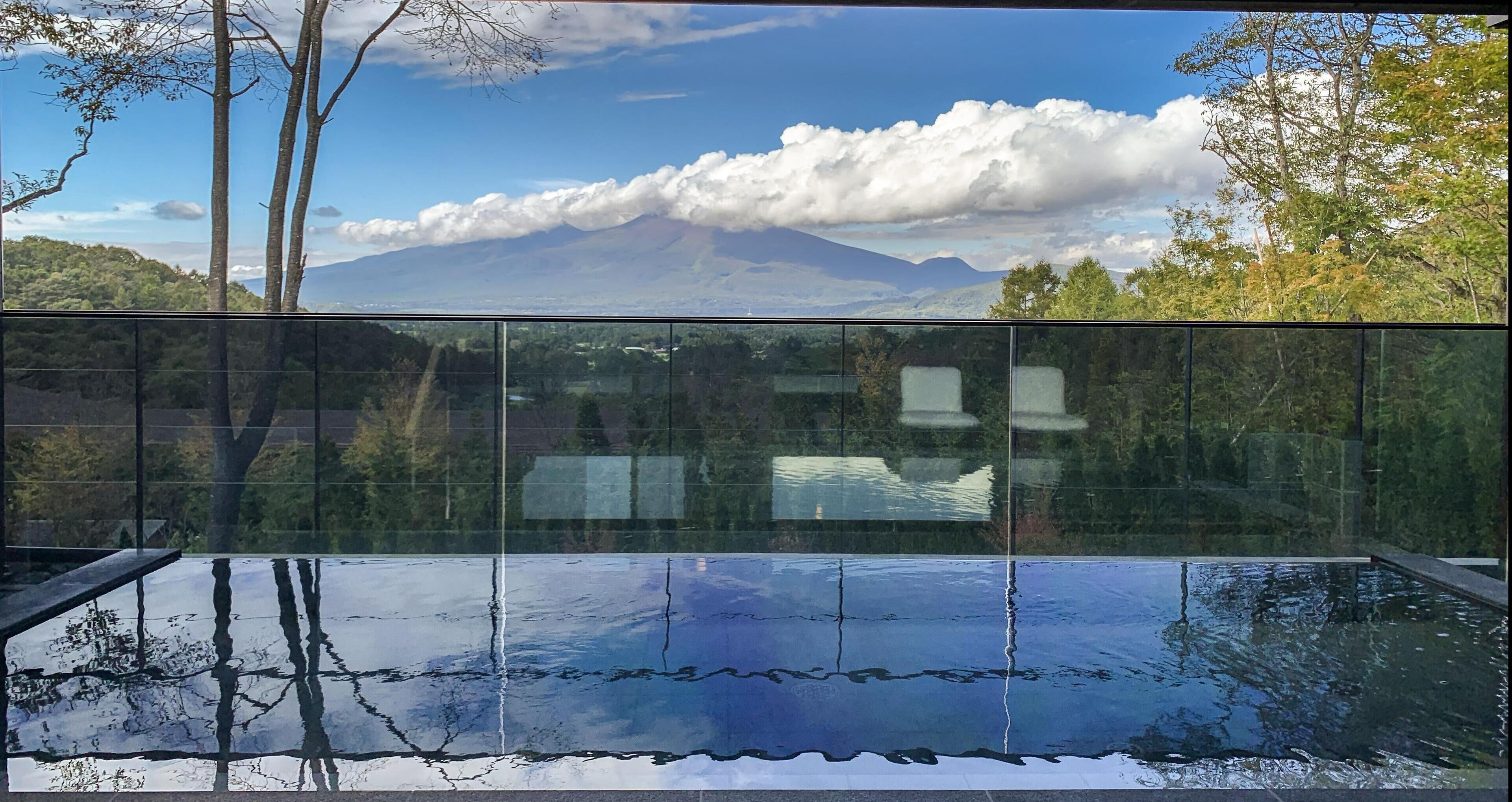 Une piscine à débordement, entourée de parois de verre, offrant une vue sur une montagne et les nuages.