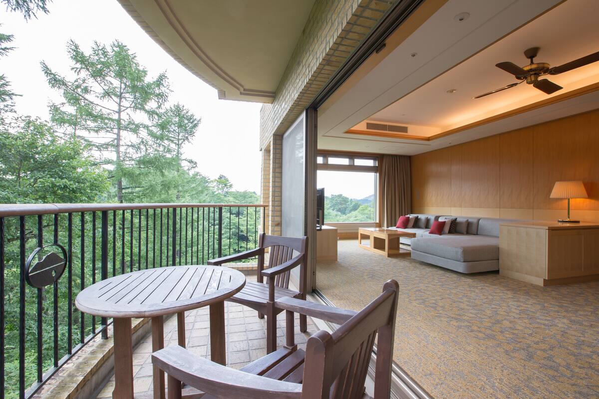 A balcony with a wooden table and chairs, a sofa, and a small table with a lamp.