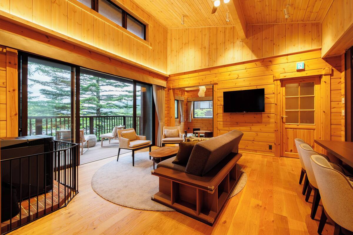 A spacious wooden cabin interior with a large sofa, chairs, a TV, and a fireplace.